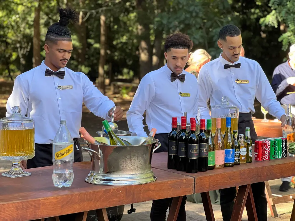 Three bartenders in white shirts and bow ties at a trestle bar with a nickel wine tub and crystal dispenser