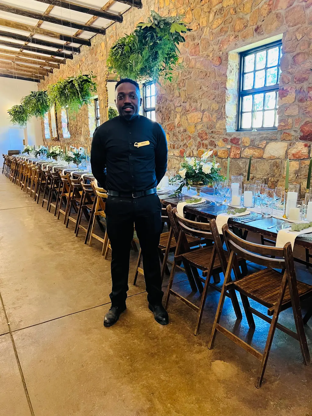 Eddie standing beside a long banquet table with hanging greenery, white flowers and green candles