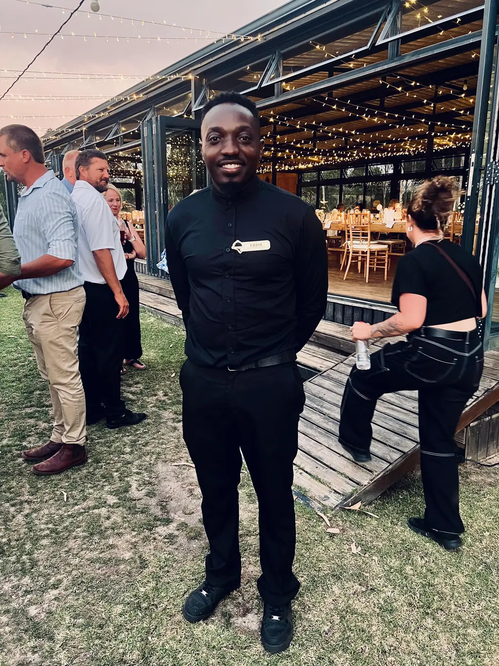 Eddie in a black uniform at dusk in front of a lit glass pavilion