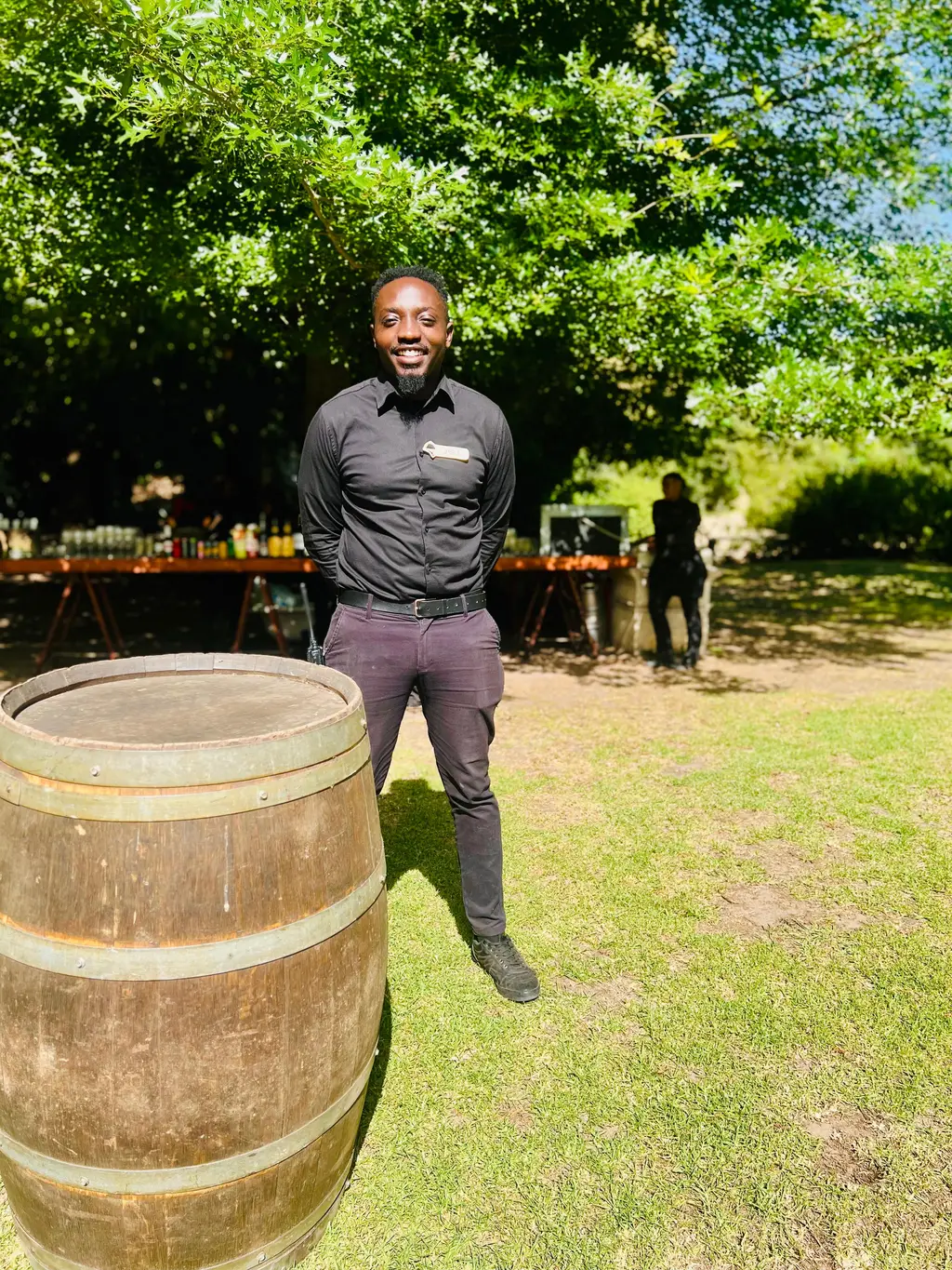 Eddie, owner of Greyt-Waitstaff, smiling next to a wine barrel in a sunny garden