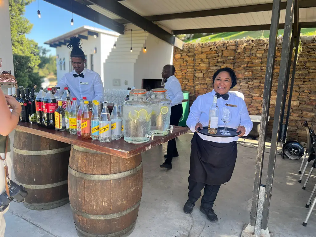 A smiling waitress carrying a tray of rosé past a barrel bar
