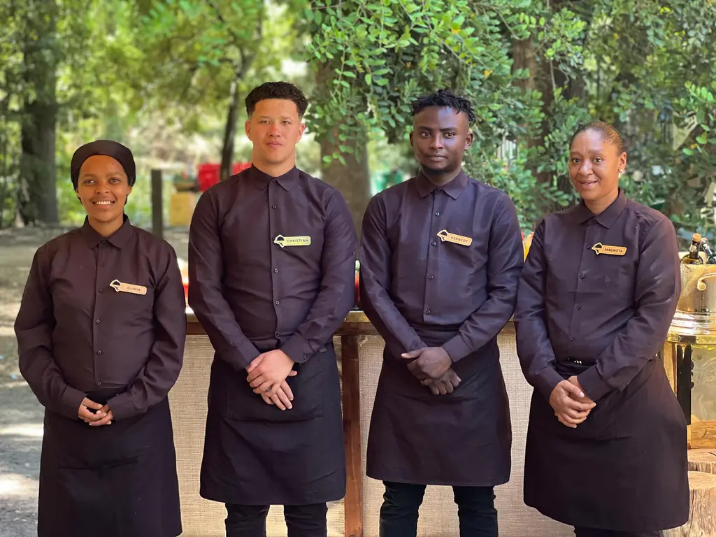 Four staff in plum shirts and aprons standing in front of a brass bar