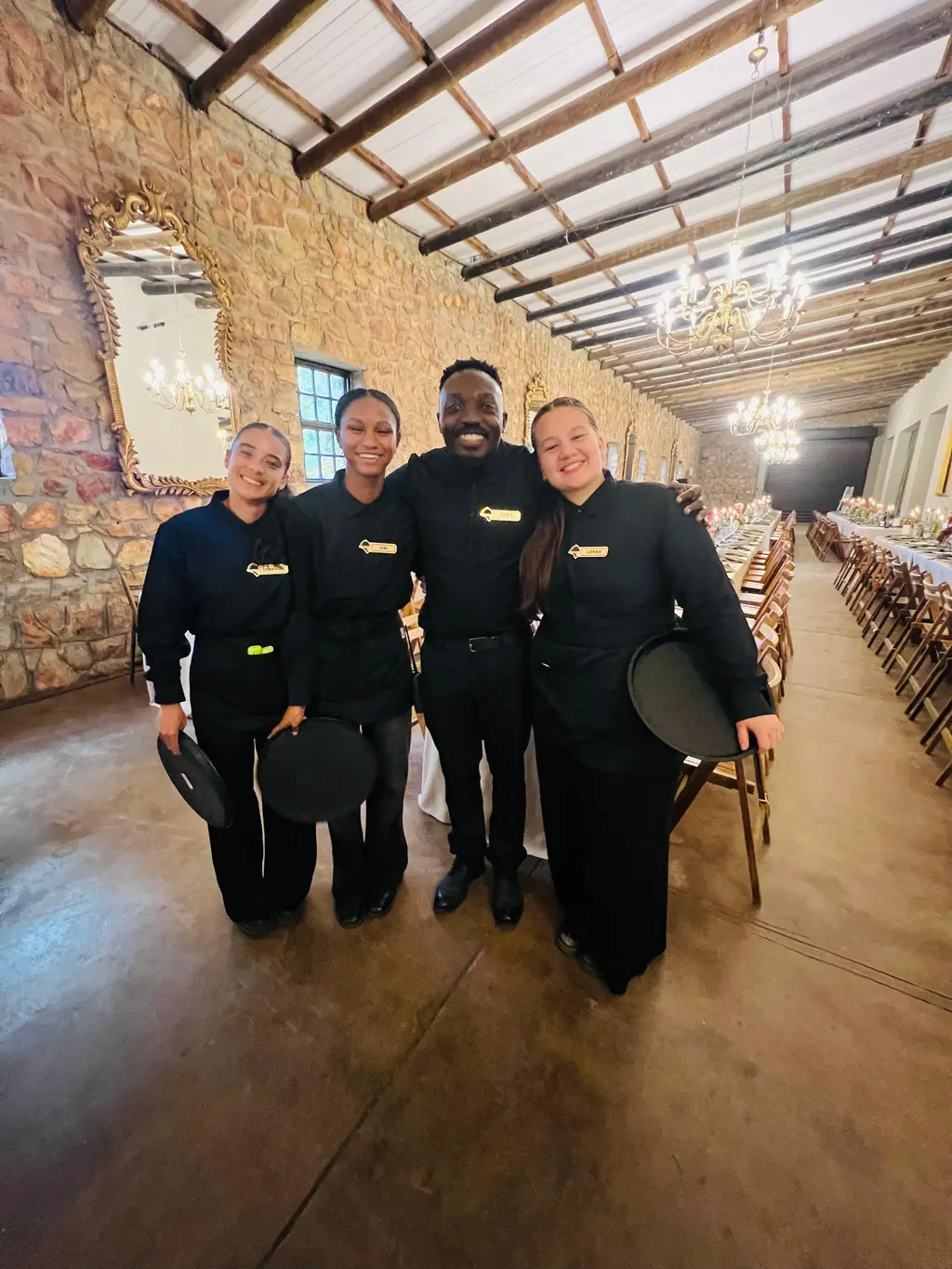 Four staff holding round serving trays in a stone hall with chandeliers